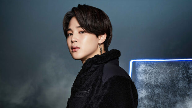 Jimin wearing a black jacket with an earring posing against a dark background