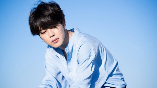 Jimin wearing a light blue shirt posing thoughtfully against a clear blue sky