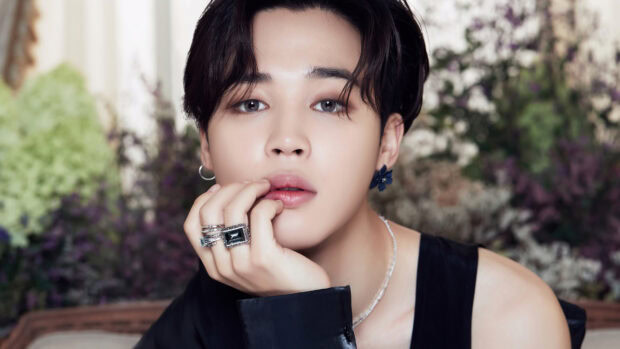 Jimin with stylish rings and earrings posing thoughtfully in a floral setting
