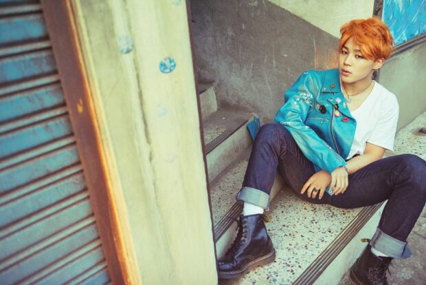 Jimin wearing a blue jacket sitting on stairs in an urban setting