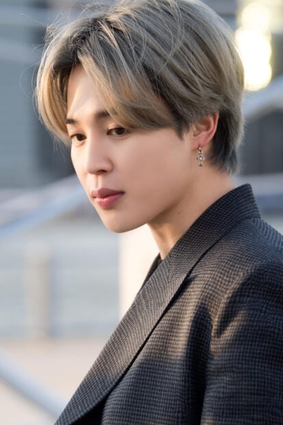 Close up of Jimin with blonde hair wearing a checkered suit jacket and cross earring