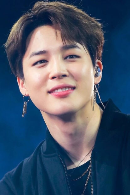 Jimin wearing earrings and smiling on stage during a concert