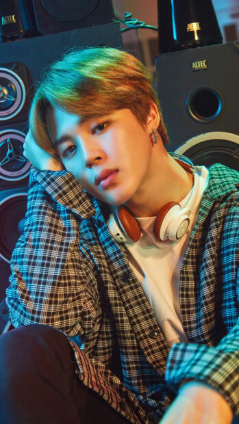 Jimin wearing headphones and a plaid shirt in a relaxed pose