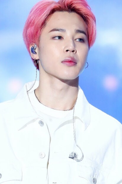 Jimin with pink hair wearing white jacket during a performance on stage