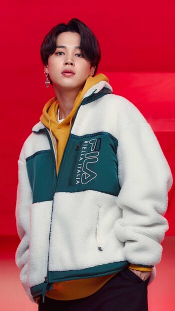 Jimin wearing a fleece jacket and hoodie posing against a red background