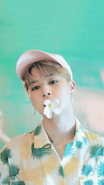 Jimin wearing a tropical shirt and pink cap with a white flower in his mouth