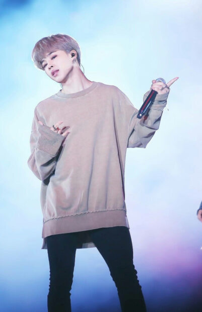 Jimin wearing a beige sweatshirt performing on stage with a microphone in hand