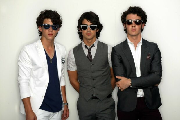 The Jonas Brothers wearing stylish sunglasses and formal outfits in a group portrait