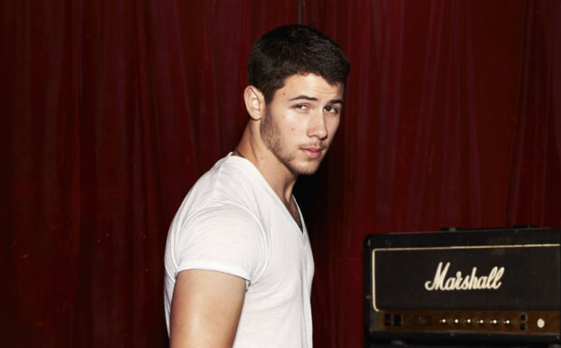 Young man wearing white t shirt posing in front of a Marshall amplifier with a red curtain background