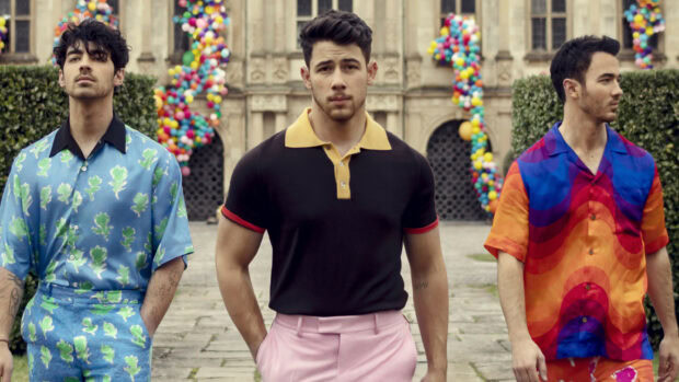 Jonas Brothers posing outdoors wearing colorful outfits in front of a decorated building