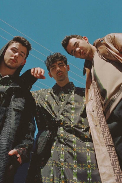 Jonas Brothers standing confidently outdoors under clear blue sky