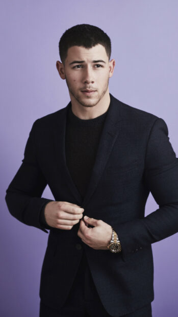 A stylish portrait of Jonas Brothers member adjusting his suit jacket against a purple background