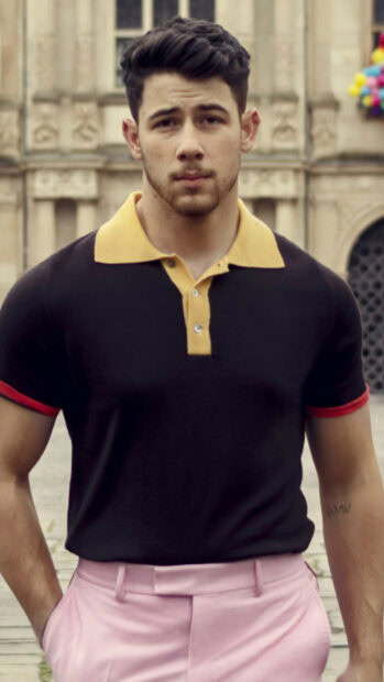 Jonas Brothers member standing outdoors wearing a black shirt with yellow collar and pink pants