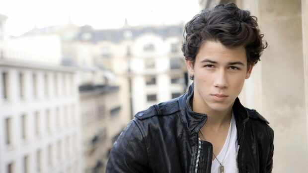 Young man from Jonas Brothers wearing a black leather jacket standing outdoors in an urban setting