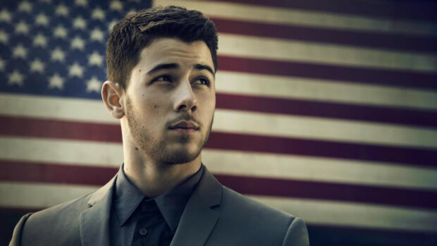 A close up of Jonas Brothers member standing in front of an American flag background