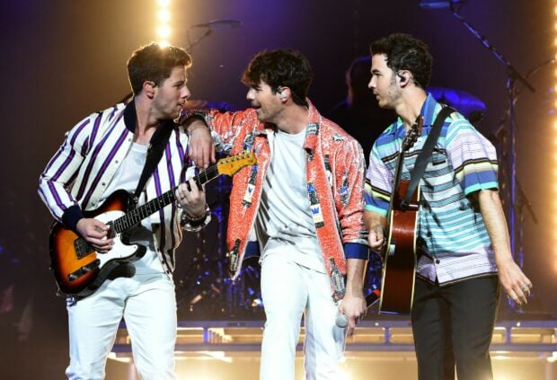Jonas Brothers performing on stage with guitars and microphone in a live concert setting