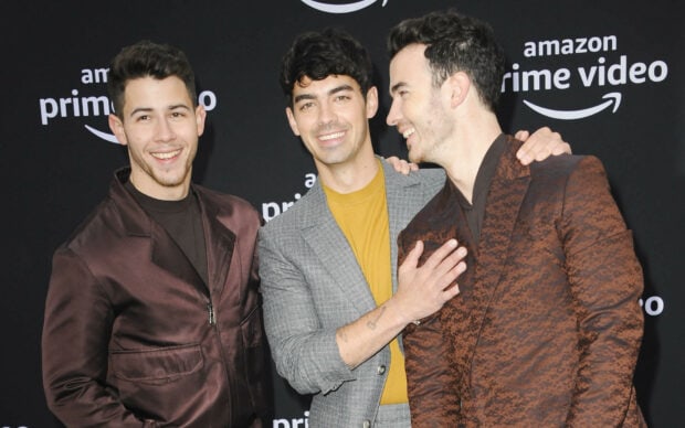 The Jonas Brothers smiling and posing together on the red carpet at an event