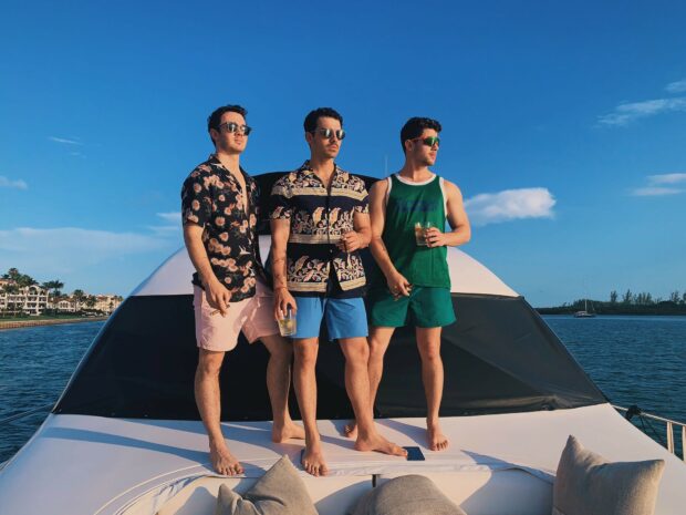The Jonas Brothers standing on a boat enjoying a sunny day outdoors
