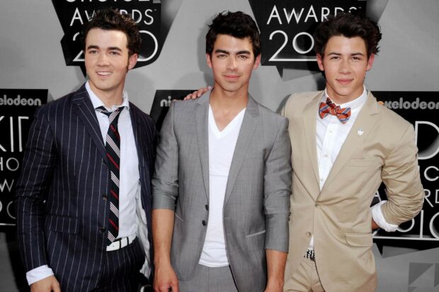 The Jonas Brothers standing together at an awards event wearing stylish suits