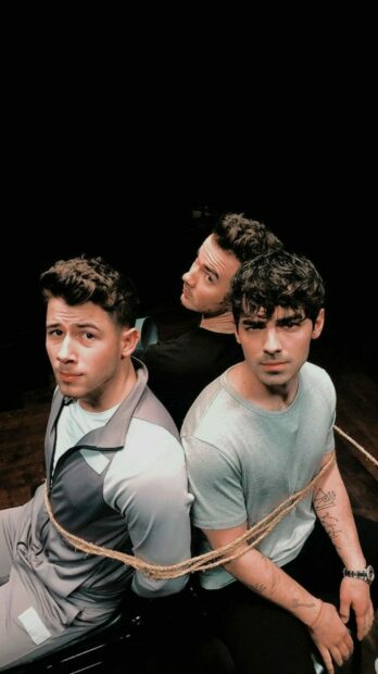 Jonas Brothers sitting tied with rope looking serious in an artistic setting