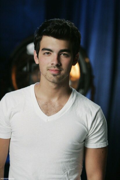 Close up of Jonas Brothers member wearing a white shirt with dark hair and light facial hair