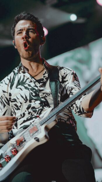 Male Jonas Brothers musician playing guitar on stage during concert