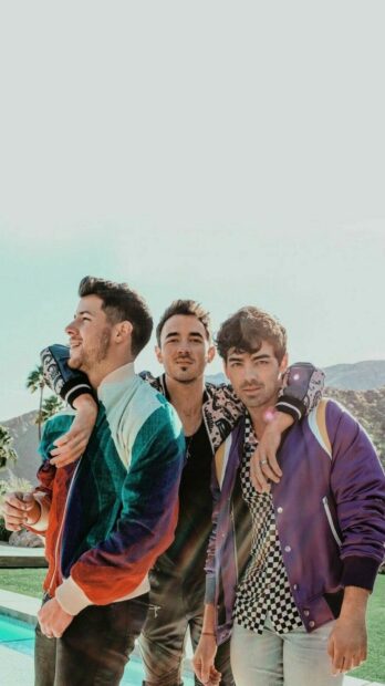 Jonas Brothers standing together outdoors with scenic mountains in the background