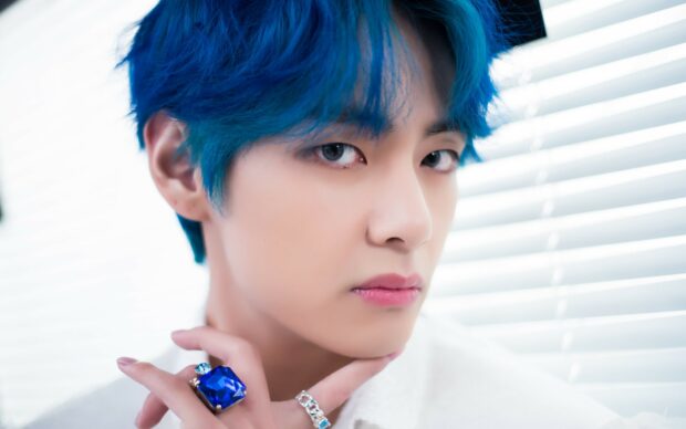 Jungkook with blue hair and blue gemstone ring posing near window blinds