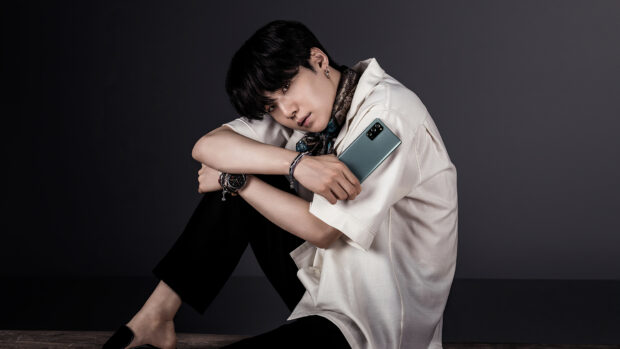 Jungkook sitting with a smartphone wearing a white shirt and black pants in a studio setting