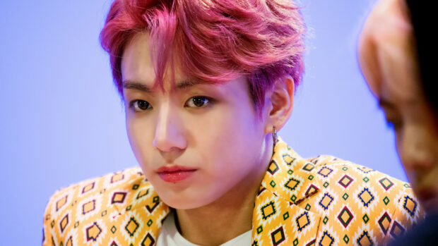Jungkook with pink hair wearing a patterned yellow jacket in a close up portrait