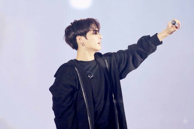 Jungkook is performing on stage wearing a black hoodie and holding a microphone in his hand