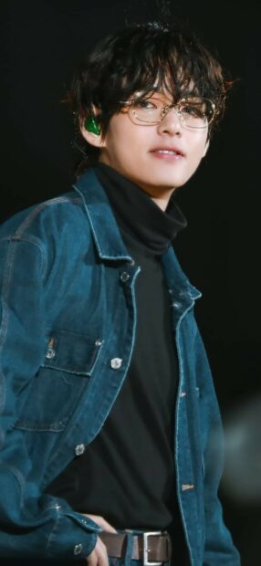 Jungkook wearing a denim jacket and glasses on stage with curly hair