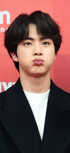 Jungkook making a cute face with puffed cheeks on a red background