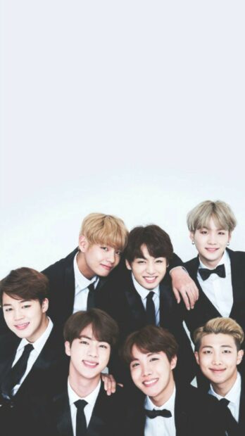 Jungkook smiling with BTS members dressed in black suits and ties
