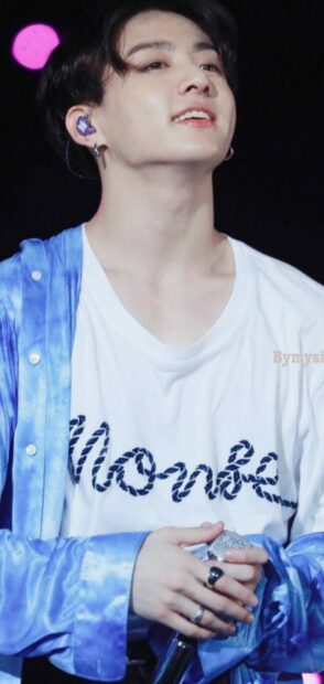 Jungkook wearing a blue shirt and holding a microphone during a live performance