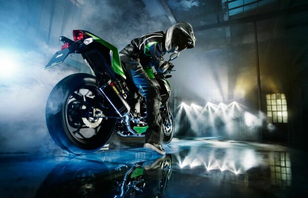 A Kawasaki rider performing a burnout with a green motorcycle in an industrial setting