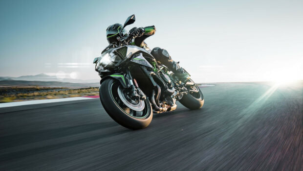 A Kawasaki motorcycle leaning sharply on a racetrack during a fast turn at sunset