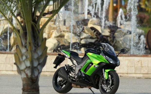A Kawasaki motorcycle parked near a fountain with rocks in the background