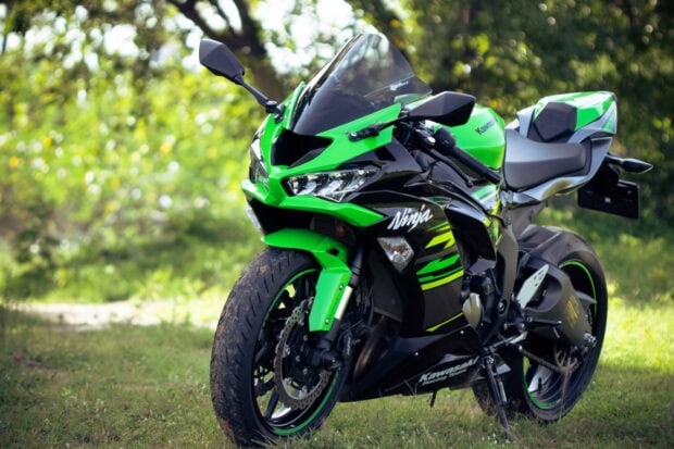 A Kawasaki sport motorcycle is parked on the grass surrounded by trees in a natural setting