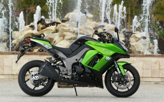 A green Kawasaki motorcycle parked in front of a stone fountain with water jets