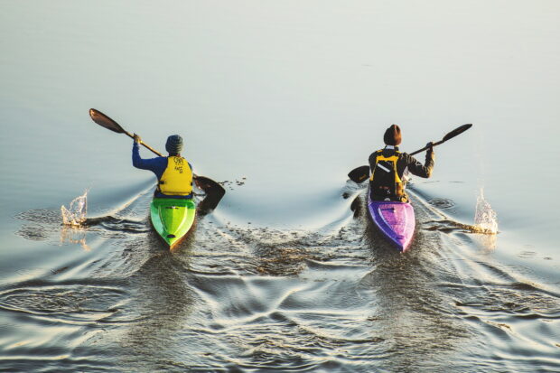 Two people kayaking side by side on calm water wearing life jackets