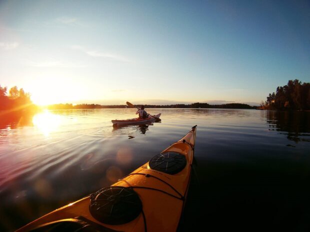 A person kayaking on calm water during sunset with a clear sky and scenic surroundings