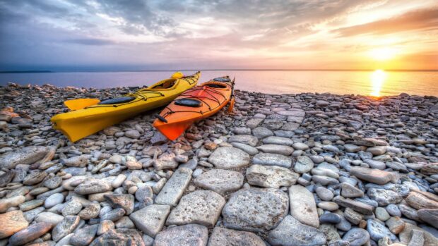 Two colorful kayaks resting on rocky shore at sunset with calm water and sky in background
