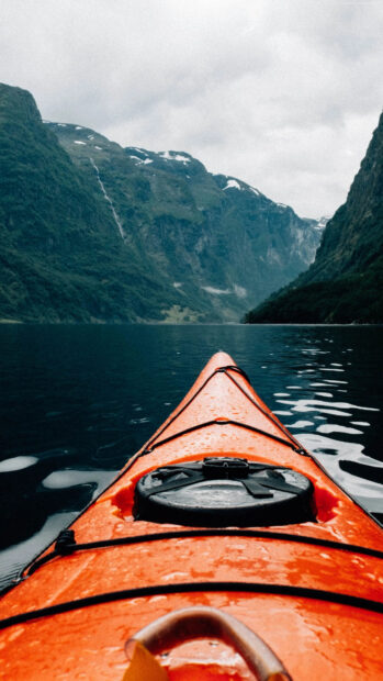 Orange kayak on calm water surrounded by green mountains during kayaking adventure