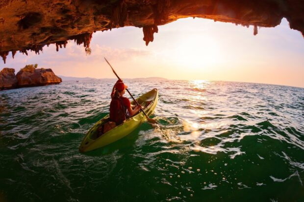 A person kayaking through a sea cave with scenic ocean views at sunset