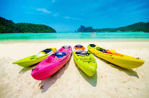 Four colorful kayaks lined up on a sandy beach near clear turquoise water