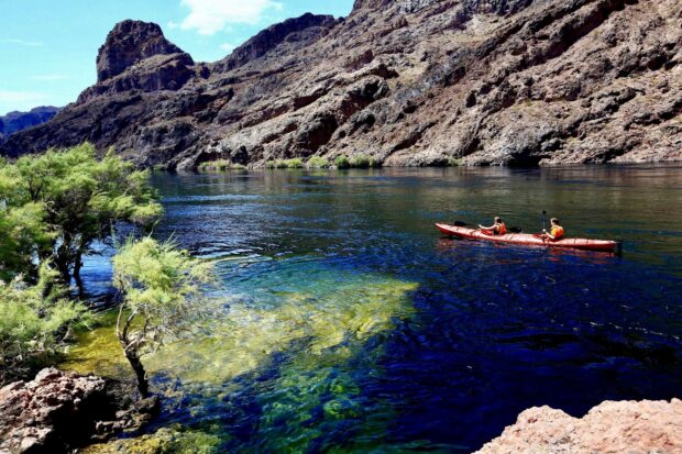 Two people kayaking on clear water near rocky canyon walls