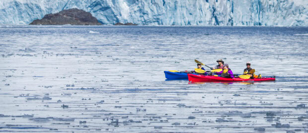 A group of people kayaking on icy water near a glacier with scattered ice chunks