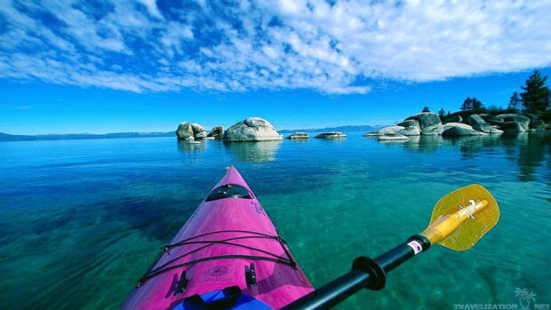 A kayak in clear water surrounded by rocks under a blue sky with clouds