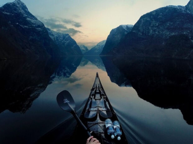A kayaking trip through calm water surrounded by towering mountains at dusk